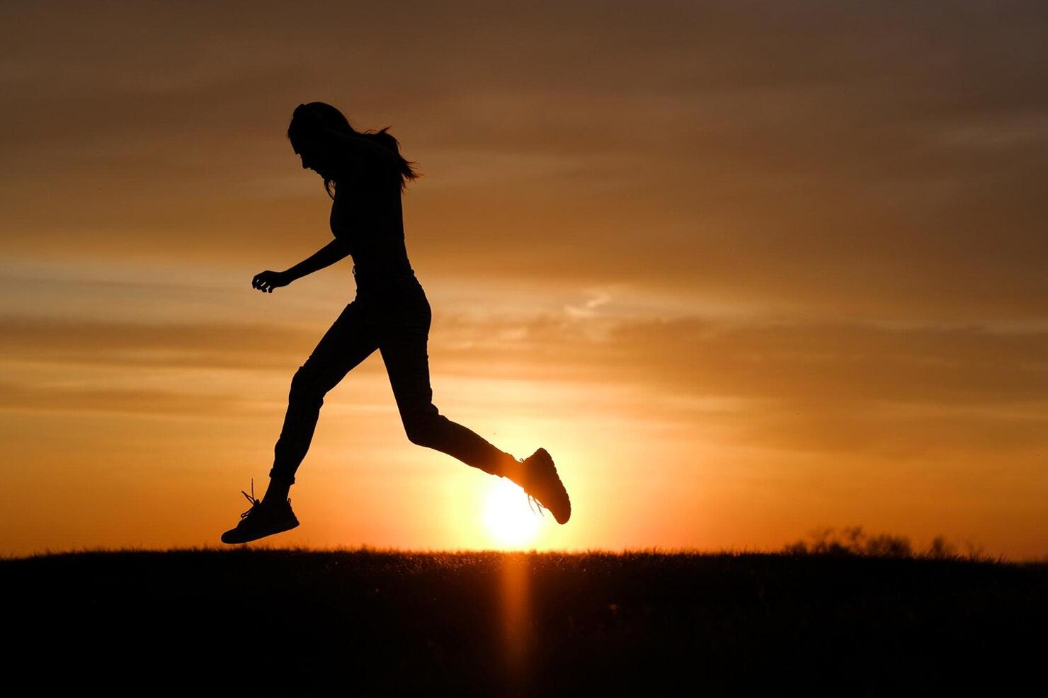 Depiction shows that a girl is running on the grass with full of energy at the time of sunset.